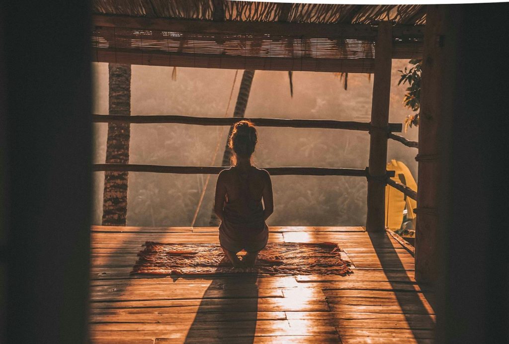 woman meditating on floor with overlooking view of trees